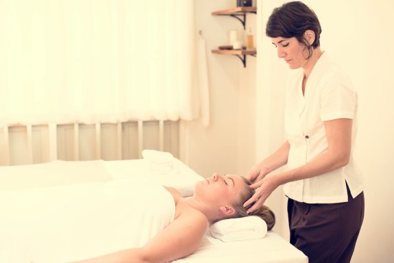 Une praticienne effectue un massage de la tête sur une personne allongée.